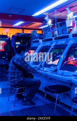 Man playing arcade games in Tokyo, Japan, surrounded by glowing blue neon lights in a classic Japanese game center. Stock Photo