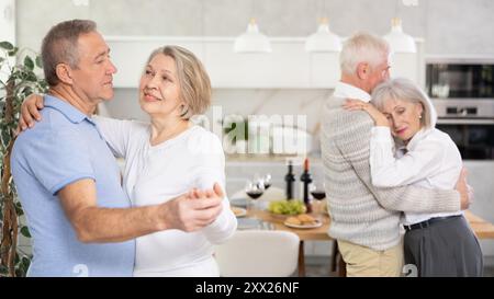 Two married couples enjoying slow dancing at house party for friends Stock Photo