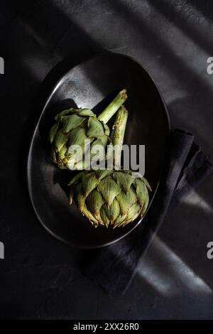 Overhead view of two artichokes in a bowl on a folded napkin in sunlight Stock Photo