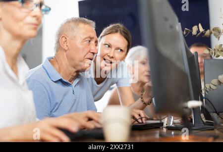 Young female mentor explaining something to elderly man during computer class Stock Photo