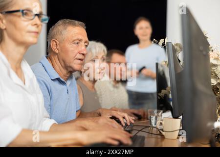 Old man learning computer programs and teacher speaking on the background Stock Photo