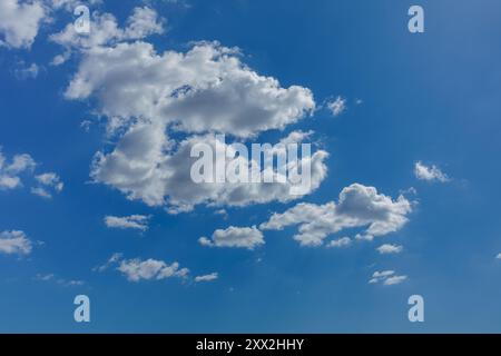 The sunlight subtly illuminates the clouds floating through a clear blue sky, casting gentle shadows and creating texture within the cluster. Stock Photo