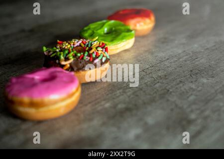Four mini donuts with different colors and sprinkles on top. The mini donuts are arranged in a row on a counter Stock Photo