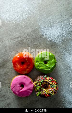 Four mini donuts with different colors and sprinkles on top. The mini donuts are arranged in a square formation Stock Photo