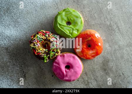 Four mini donuts with different colors and sprinkles on top. The mini donuts are arranged in a square formation Stock Photo