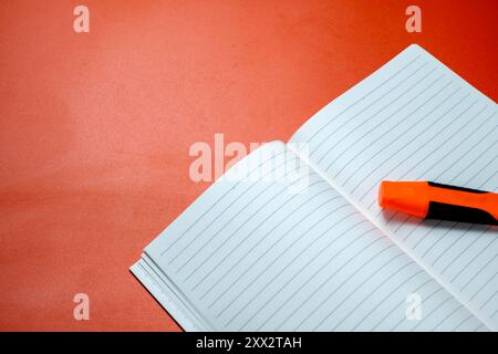 A notebook is open on a red table. The notebook is white and has a few lines drawn on it Stock Photo