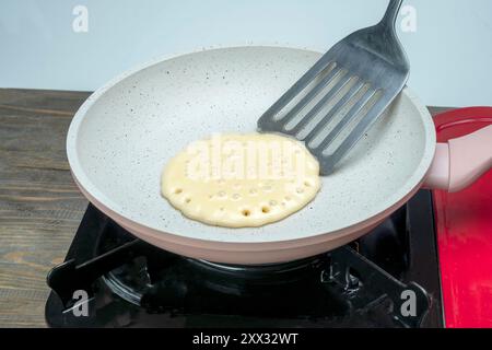 A pancake is being cooked in a pan on a stove. The pancake is in the process of being flipped with a spatula Stock Photo