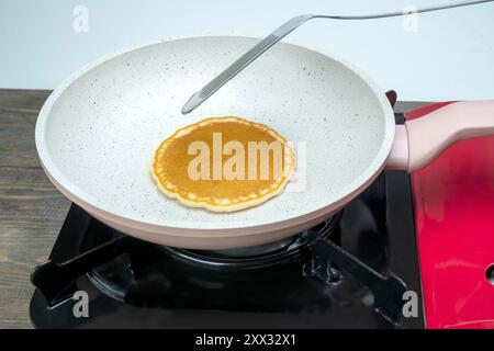 A pancake is being cooked in a pan on a stove. The pancake is in the process of being flipped with a spatula Stock Photo