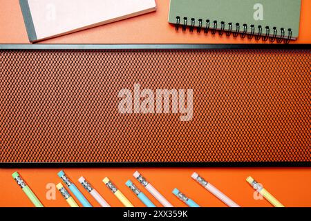 A table with a brown background and a bunch of pencils and notebooks. The pencils are in different colors and sizes, and the notebooks are of various Stock Photo