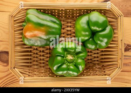 Three sweet green peppers with straw tray on wooden table, macro, top view. Stock Photo