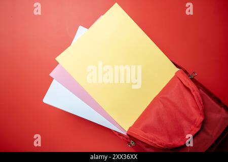 A red backpack with three sheets of paper inside. The backpack is open and the papers are yellow Stock Photo