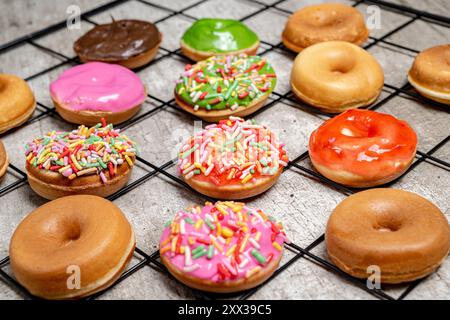 A tray of assorted mini donuts with sprinkles and frosting. The mini donuts are of different colors and flavors, and they are arranged in a grid patte Stock Photo