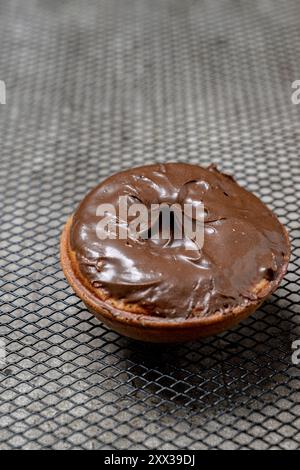 A chocolate mini donut sits on a metal mesh. The mini donut is covered in chocolate and he is freshly made Stock Photo