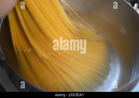 Beautiful and healthy food, food. Long Italian durum wheat vermicelli is boiled with hot water in a gray metal saucepan on a gas stove. Stock Photo