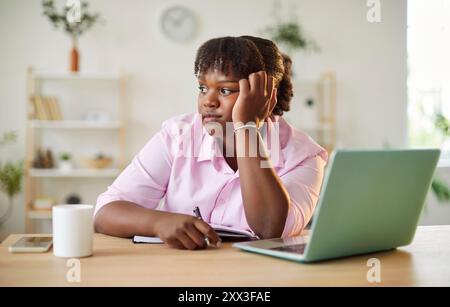 Pensive African American woman sitting at desk, thinking about work project, taking break from work. Stock Photo