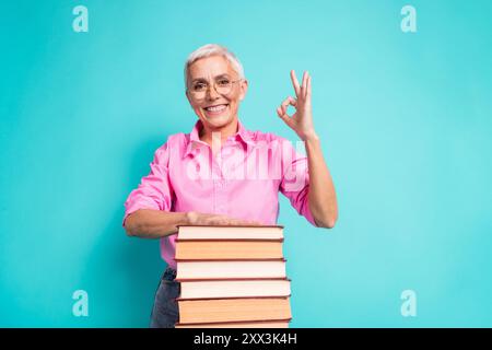Portrait of nice aged lady okey symbol book wear pink shirt isolated on turquoise color background Stock Photo