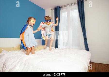 Two children in superhero outfits are jumping on a parents bed Stock Photo