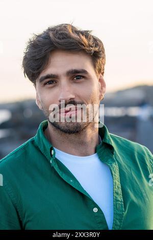 Close-up portrait of a handsome young man with beard and stylish haircut, wearing a green shirt outdoors. Image captures modern male fashion, confiden Stock Photo