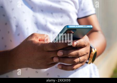 Glamorous smiling black man, sitting using a social media app on a smartphone. Stock Photo