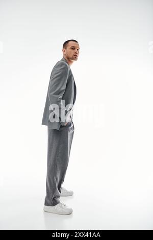 A stylish man in a grey suit stands with his hands in his pockets, looking over his shoulder. Stock Photo