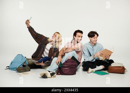 Three young people are sitting on a grey background, laughing and enjoying each others company. Stock Photo