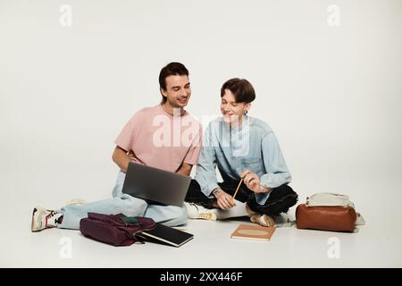 Two young queer students sit on the floor, collaborating on a project with a laptop and notebook. Stock Photo