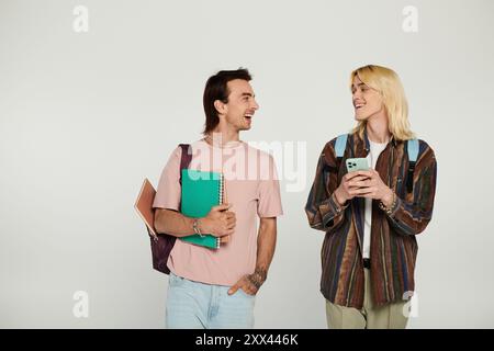 Two young people, part of the LGBTQIA community, laugh and chat while holding books and a phone. Stock Photo