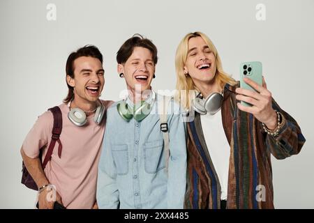 Three young, queer students laugh together while taking a selfie on a grey background. Stock Photo