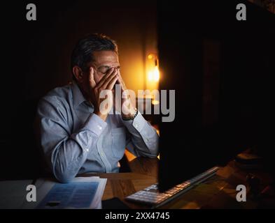 Mature businessman, headache and night with anxiety on computer for deadline, overworked or burnout at office. Tired man or frustrated employee Stock Photo