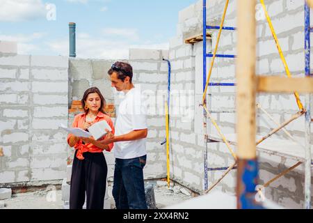 Man architect engineer shows gas block material for house construction to woman future homeowner checking blueprint plan Stock Photo