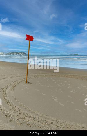 A Red sign stuck in the sand on the beach indicates a dangerous area in the sea so that swimmers do not enter this area. The Enseada Beach at Guaruja Stock Photo