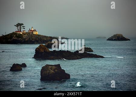 The lighthouse glows as sunset approaches and fog begins to blanket the coastline in Crescent City, California. Stock Photo