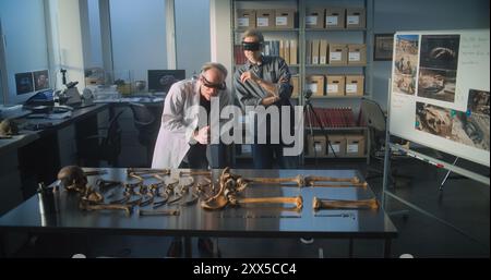 Two archaeologists in VR headsets study remains of ancient extinct human skeleton using augmented reality technology. Scientists doing historical research while working in modern archaeological lab. Stock Photo