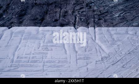 Climate | Albedo | Rhone: Huge fleece blankets cover parts of the Rhone Glacier in Switzerland in an attempt to stall the inevitable melting of the snow and ice. After a winter with record amounts of snow, most of it was gone when this image was taken on July 14th 2018, exposing the darker ice. While snow is a brilliant reflector of the energy from the sun, the darker ice absorbs the energy instead, accelerating the melting of the glacier. The color and darkness of glacier ice vary all over the world, depending on build-up of pollution, age of the ice, particles picked up by the ice and by mic Stock Photo