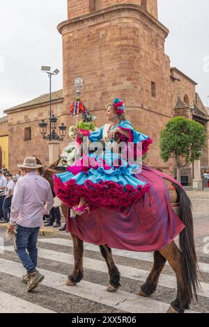 Andujar, Jaen Province, Andalusia, Spain. April 29, 2023. Woman in traditional dress riding a horse side saddle in a procession at a religious festiva Stock Photo