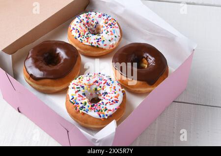 Closeup of a pink bakery box with four fresh donuts, two chocolate and two frosted with sprinkles. Stock Photo