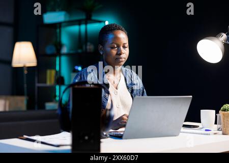 Busy female student researching online for her thesis, using her digital laptop. Dedicated african american freelancer blogging from home, utilizing modern technology for her work. Stock Photo