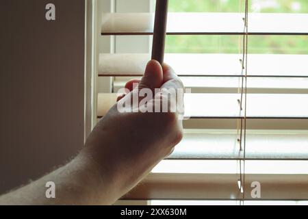 Closeup of man's hand opening window blinds to bright daylight Stock Photo
