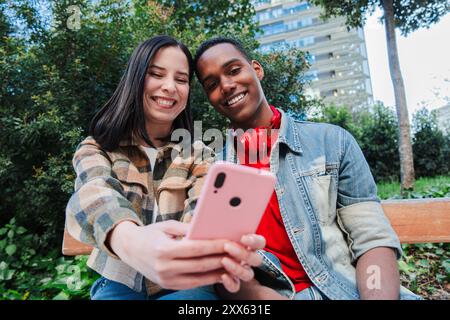 A young multiracial couple enjoys browsing the internet on a cellphone. Two teenage friends use a smartphone to share content on a social media app. Young people watch the mobile phone screen. High quality photo Stock Photo