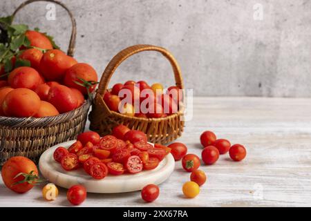 Sliced tomatoes on a white marble slab, surrounded by fresh tomatoes in baskets Stock Photo
