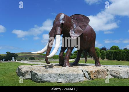 Metal sculpture of an elephant on a rock foundation in a green park under a blue sky with white clouds, Bacalhoa, Bacalhoa Buddha Eden, Quinta dos Lo Stock Photo