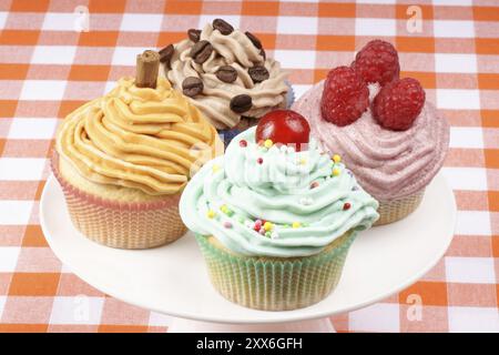Assortment of fancy cupcakes on a white porcelain cake stand. One with raspberries, one with candied cherry, one with coffee and one with carrot and c Stock Photo
