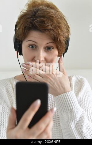 Woman in a headphones with surprise looks at smartphone Stock Photo