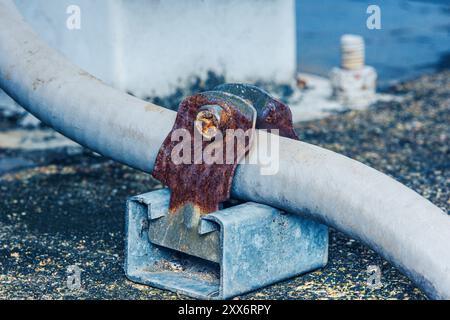 Rusty metal clamp holding electrical conduit on rooftop. Stock Photo