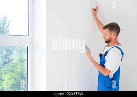 Male worker with tablet computer installing alarm system in room Stock Photo