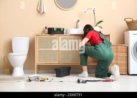 Female plumber with tools fixing sink in bathroom Stock Photo