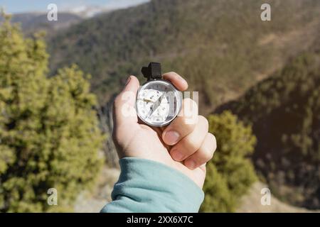 Close-up A man's hand holds a pocket compass against the backdrop of mountains and woods. The concept of outdoor navigation Stock Photo