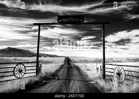 The entryway to a backcountry ranch in rural northwest Colorado. Wagon wheels accent the fence and gate. Black and white high contrast. Stock Photo