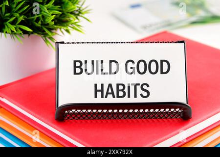 motivational reminder development concept words BUILD GOOD HABITS on a business card standing in a stand on notebooks Stock Photo