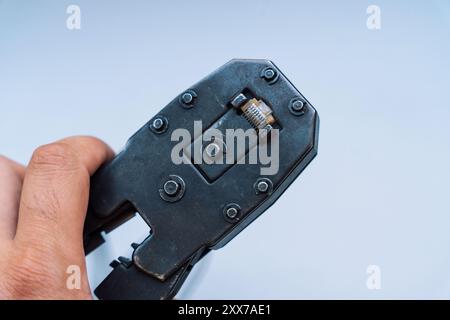 Specialist crimps connector on network cable using crimper against gray background. Stock Photo